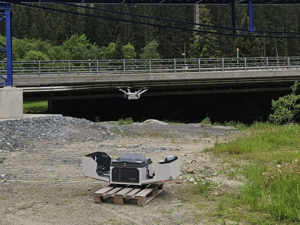 Drohne startet automatisch aus DJI Dock neben Brücke in bewaldeter Umgebung
