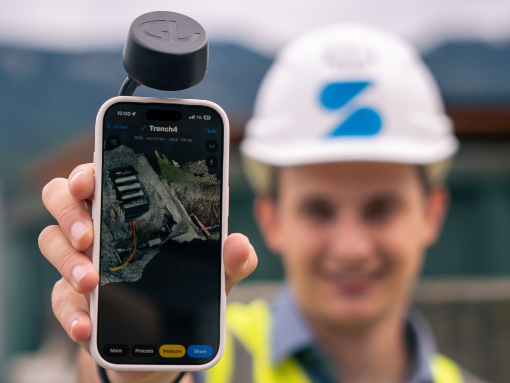 Bauarbeiter zeigt 3D-Scan einer Baustelle auf Smartphone mit GNSS-Aufsatz