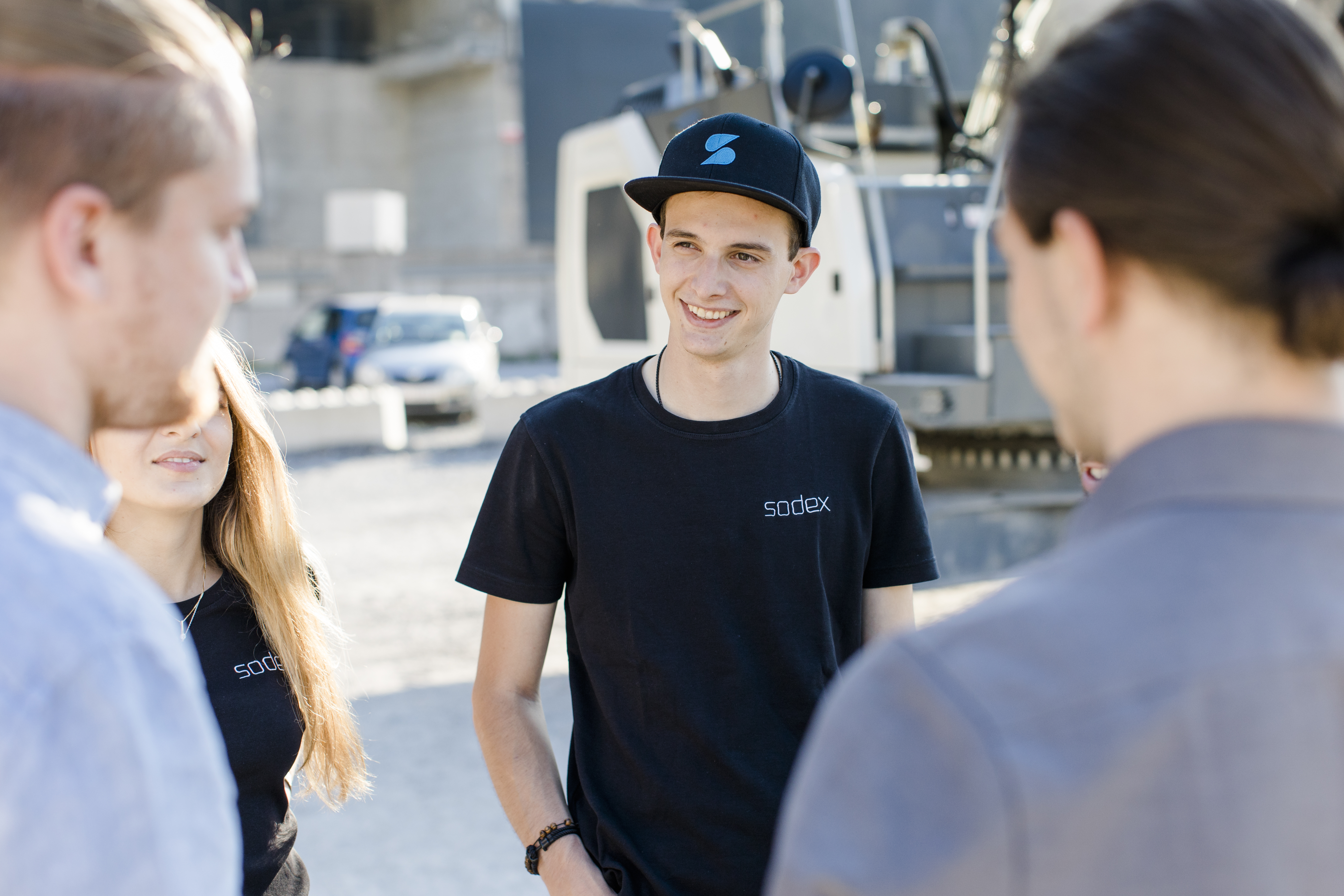 Sodex-Team im Gespräch auf Baustelle, zentraler Mitarbeiter mit Sodex-Cap im Fokus